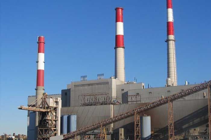 Power plant with three tall chimneys, blue sky background. Chimneys are red and white striped.