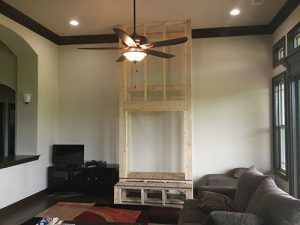 Interior room with wood-framed fireplace construction; ceiling fan, sofa, TV stand, windows, and crown molding visible.