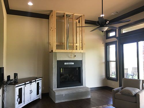 Fireplace under construction, framed in wood, with a TV cabinet and a seated chair visible.