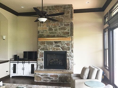 Stone fireplace with wooden mantle, a ceiling fan, and white entertainment center in a living room.