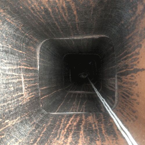 Looking up a dark, square chimney.  Smoky soot covers the interior.  A white rope hangs down.