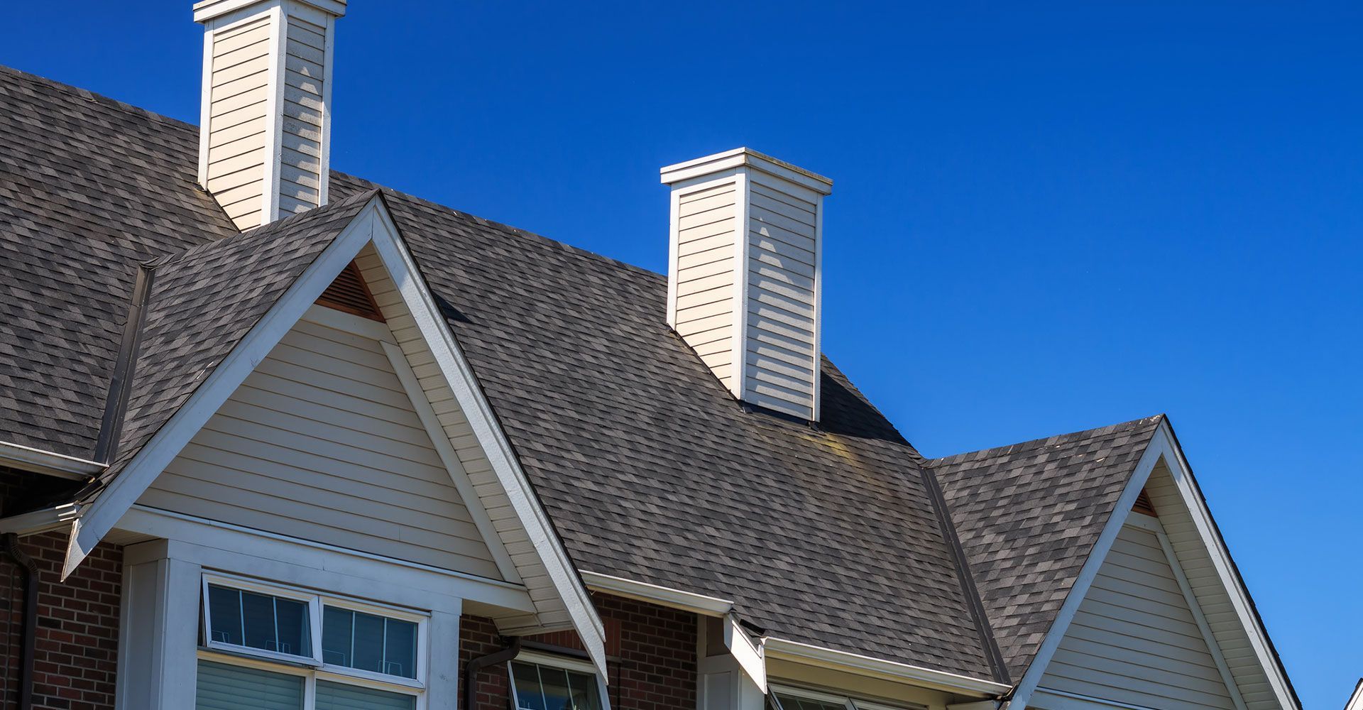 House roof with white trim and chimneys against a blue sky.
