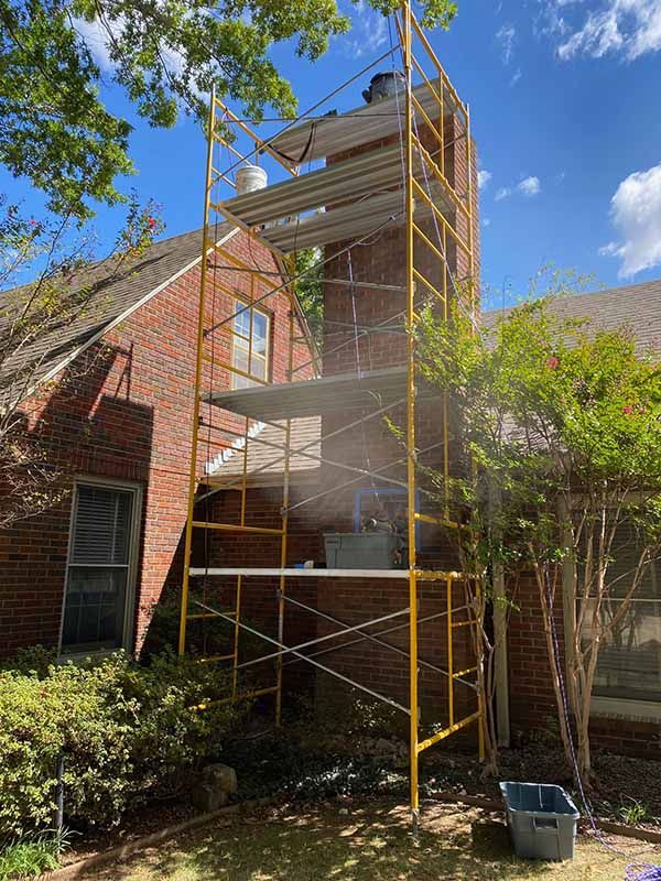 Yellow scaffolding set up against a brick chimney on a house, with buckets and materials on platforms.