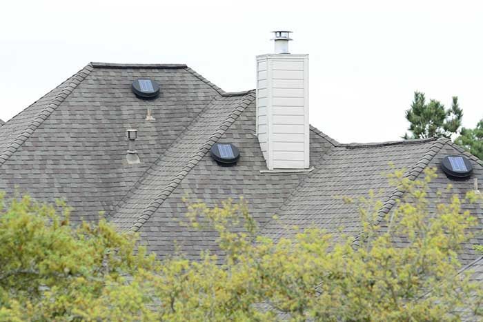 Gray shingled roof with three solar tubes and a white chimney. Trees obscure the foreground.