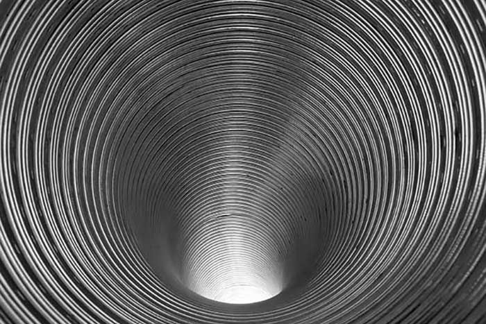 Inside view of a metallic, corrugated tube, narrowing towards a bright light.
