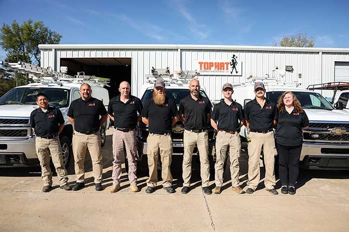 Group of people in black shirts and khaki pants standing in front of company vans.