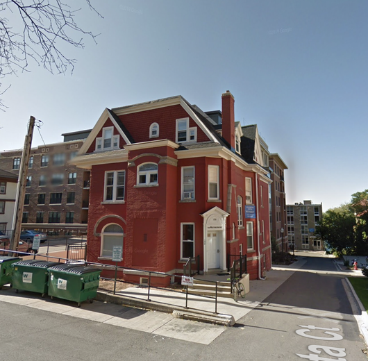 A large red brick building with a green trash can in front of it
