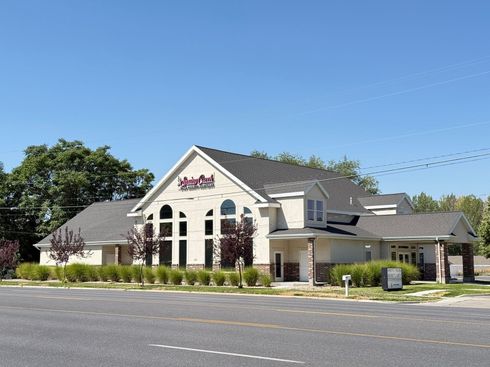 Cream-colored building with dark roof and arched windows. Road and blue sky in the background.