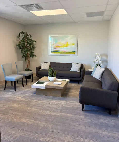 Waiting room with gray couches, chairs, and a coffee table. Large artwork on the wall.