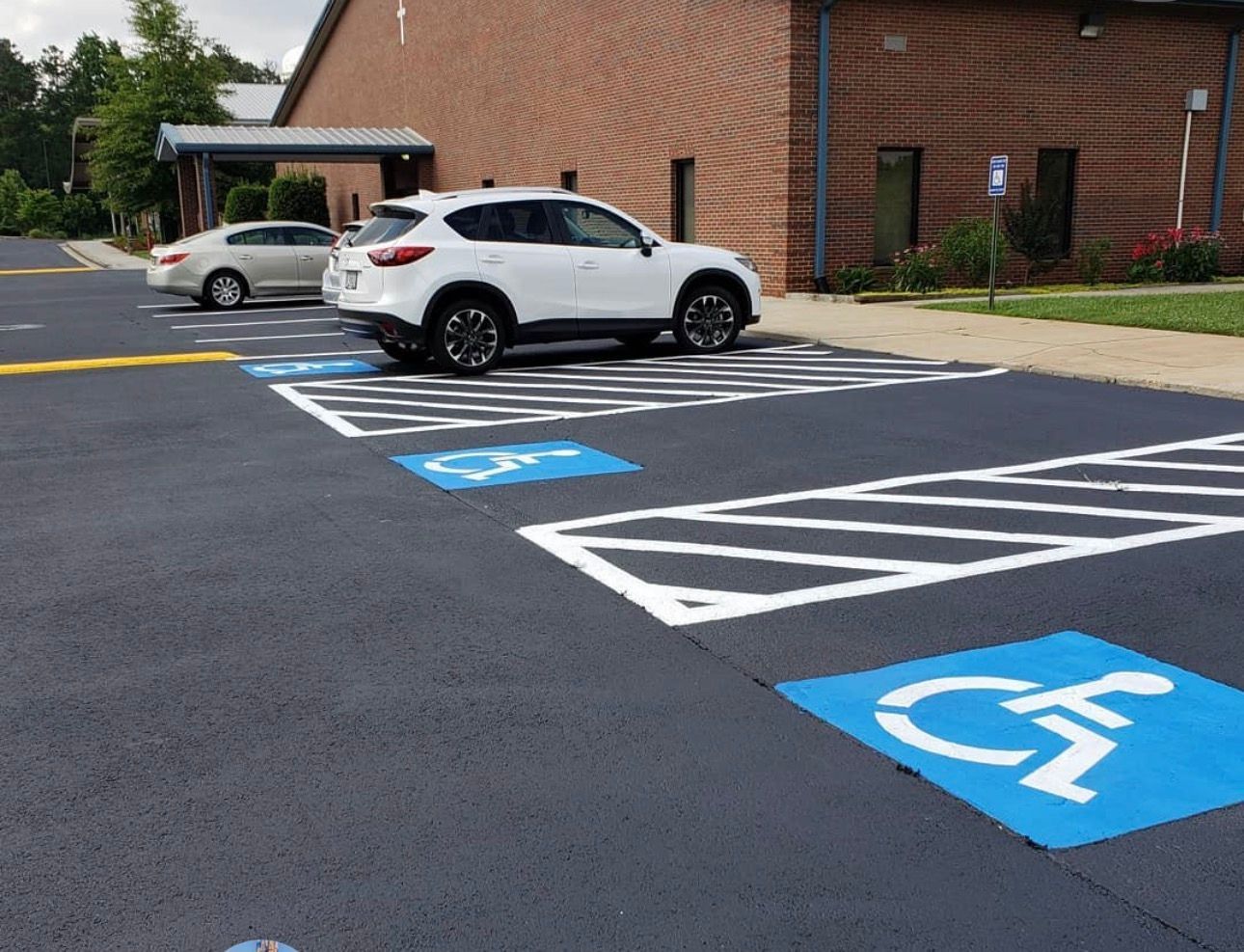 A parking lot with several painted blue handicap accessible spots, featuring white parking stripes and a parked white SUV.