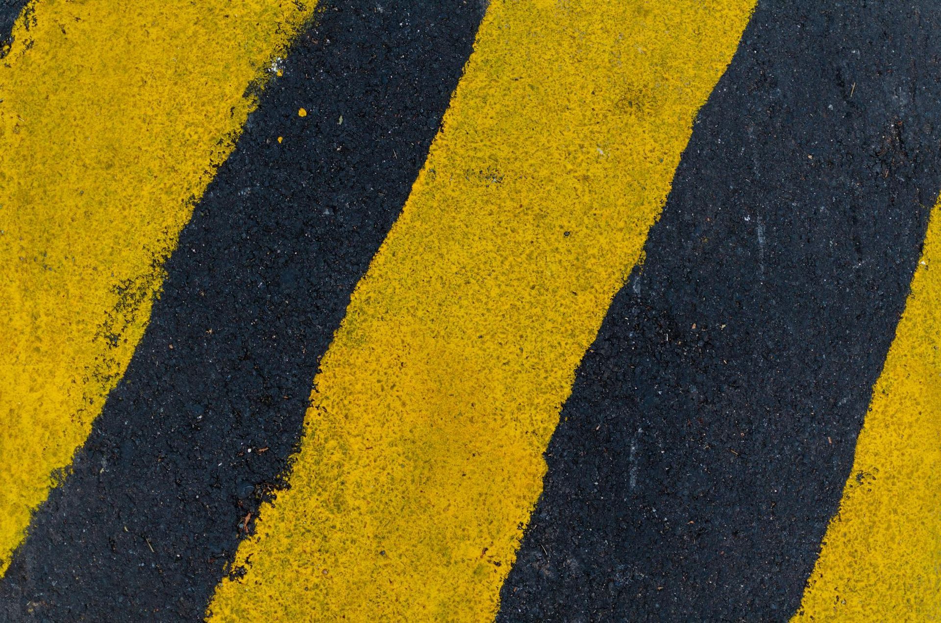 A surface with diagonal black and yellow warning stripes painted on textured asphalt.