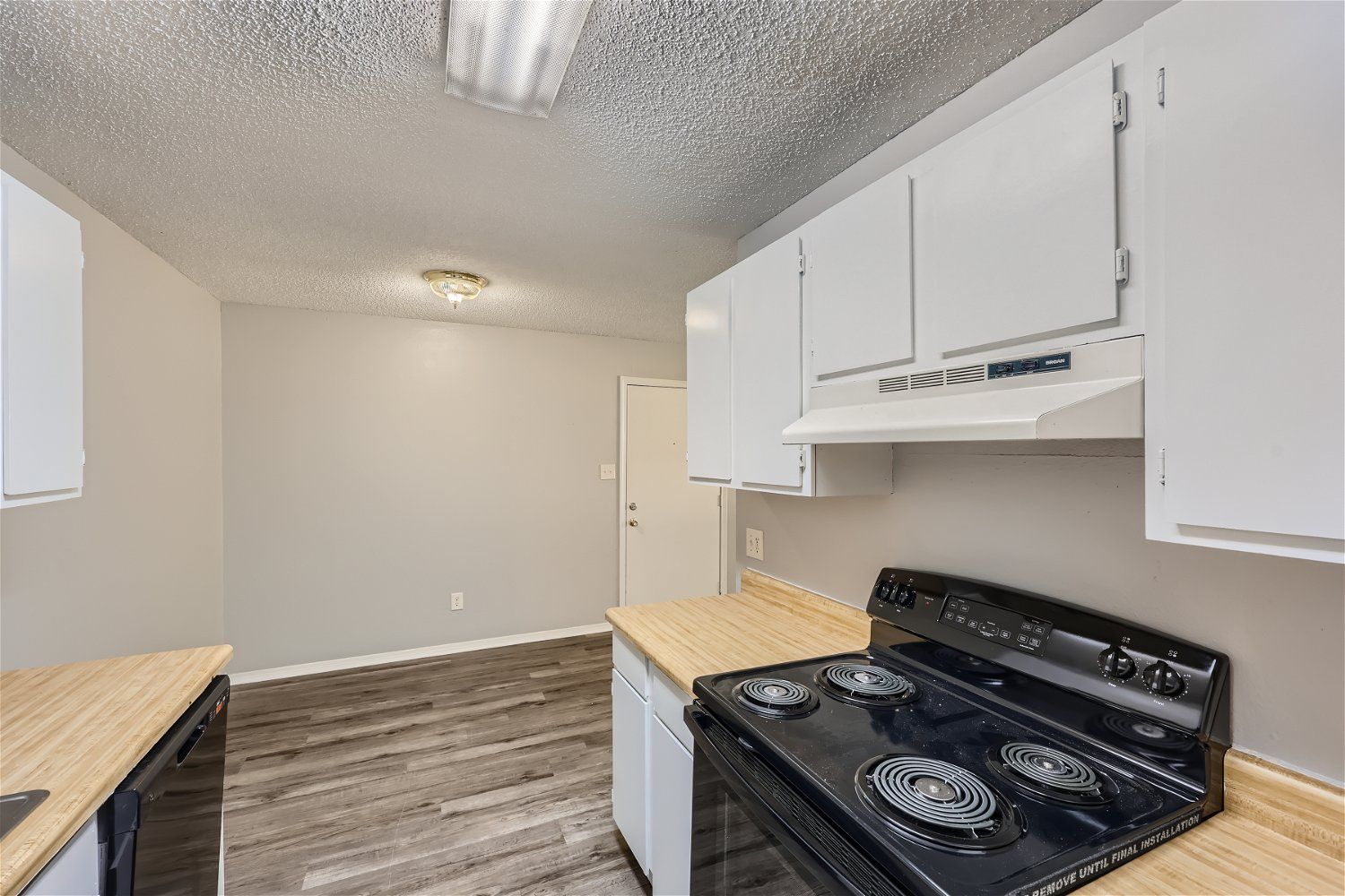 Kitchen with white cabinets, black stove, light countertops, and light gray walls.