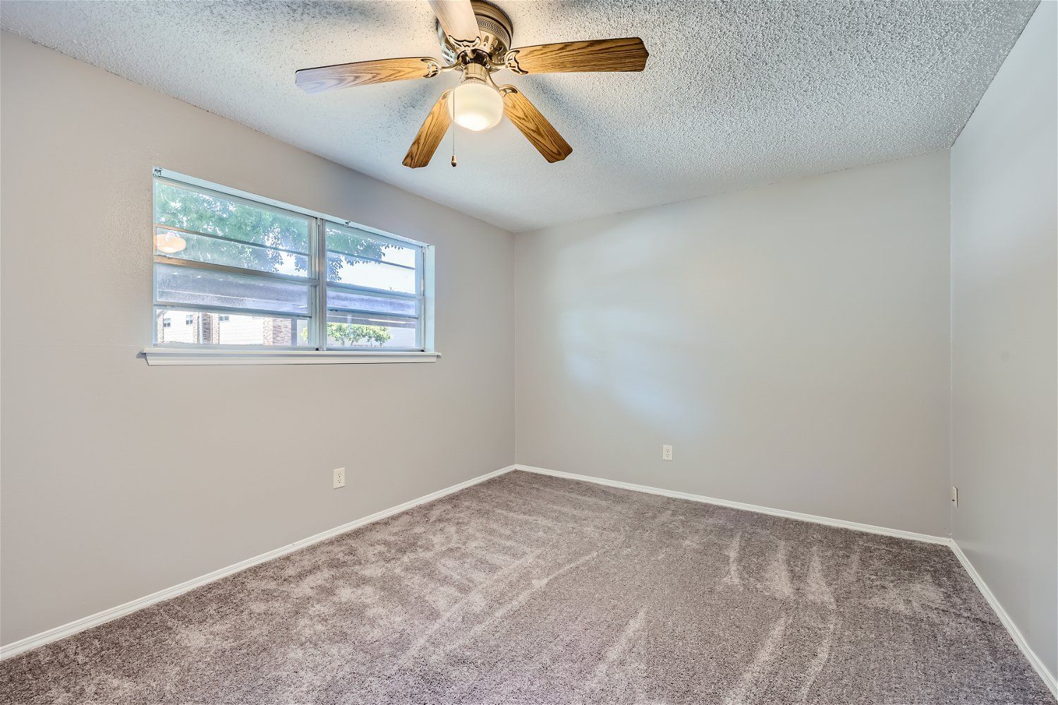Empty room with carpet, window, and ceiling fan. Light gray walls.