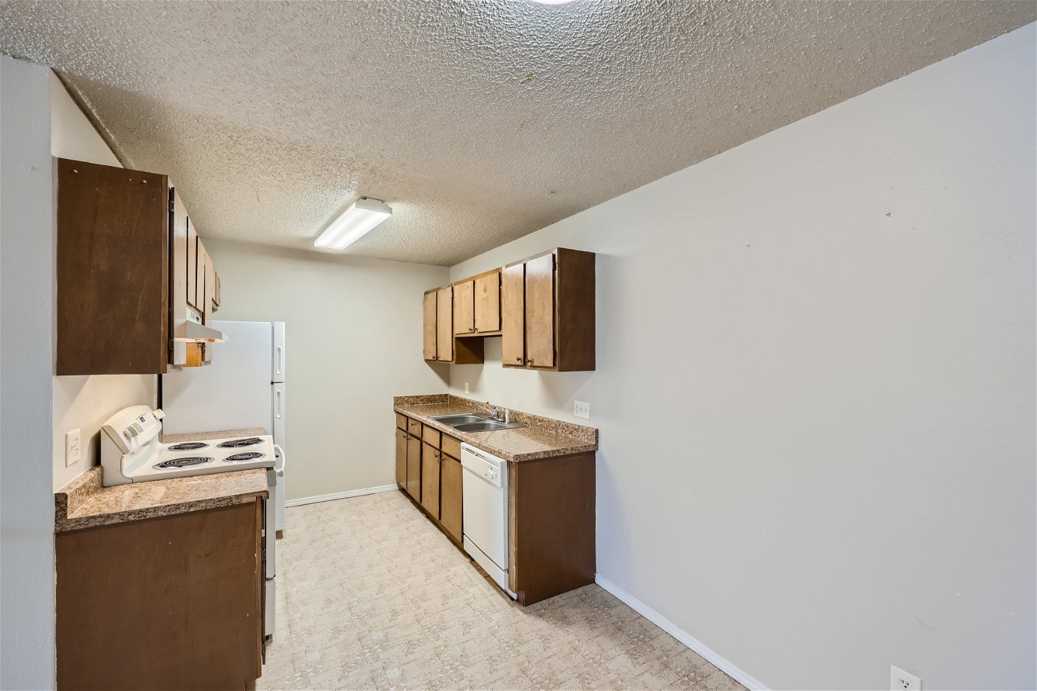 Kitchen with brown cabinets, white appliances, and beige countertops, empty room.