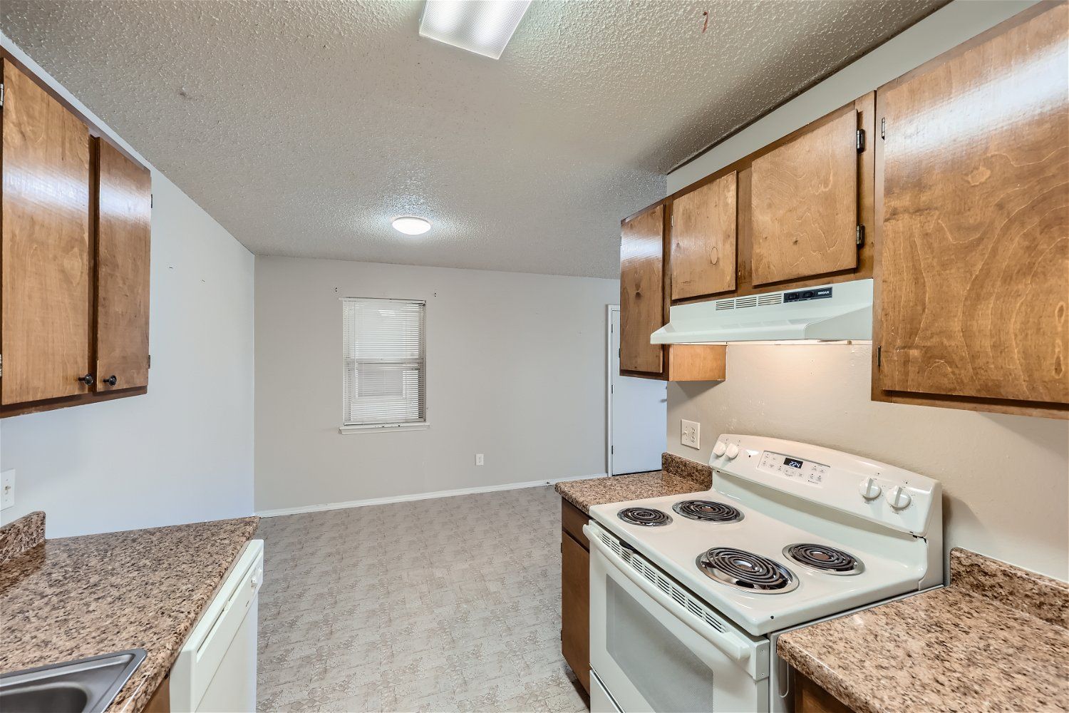 Kitchen with wooden cabinets, white appliances, and speckled countertops.