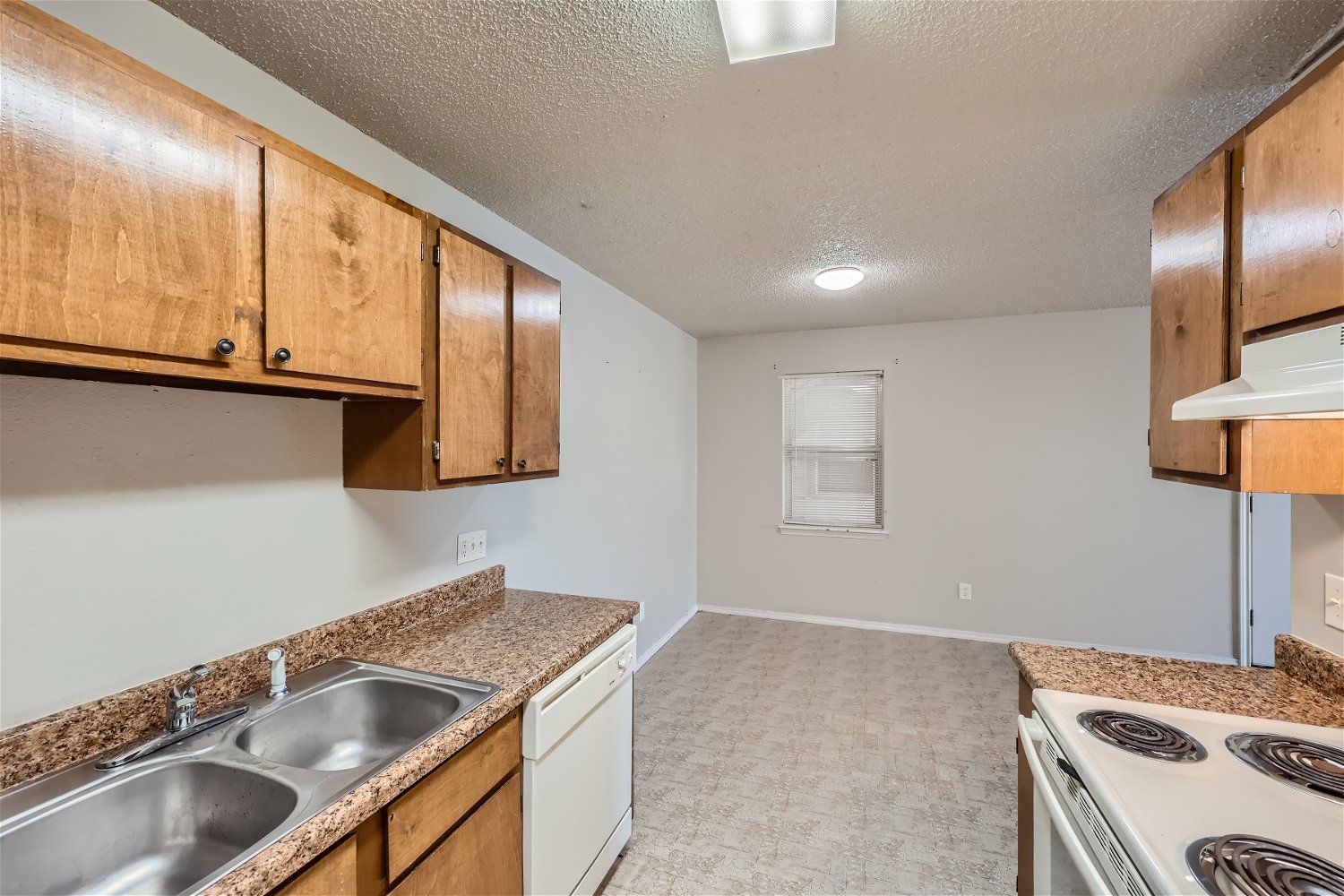 Kitchen with wood cabinets, double sink, white appliances, and a window.