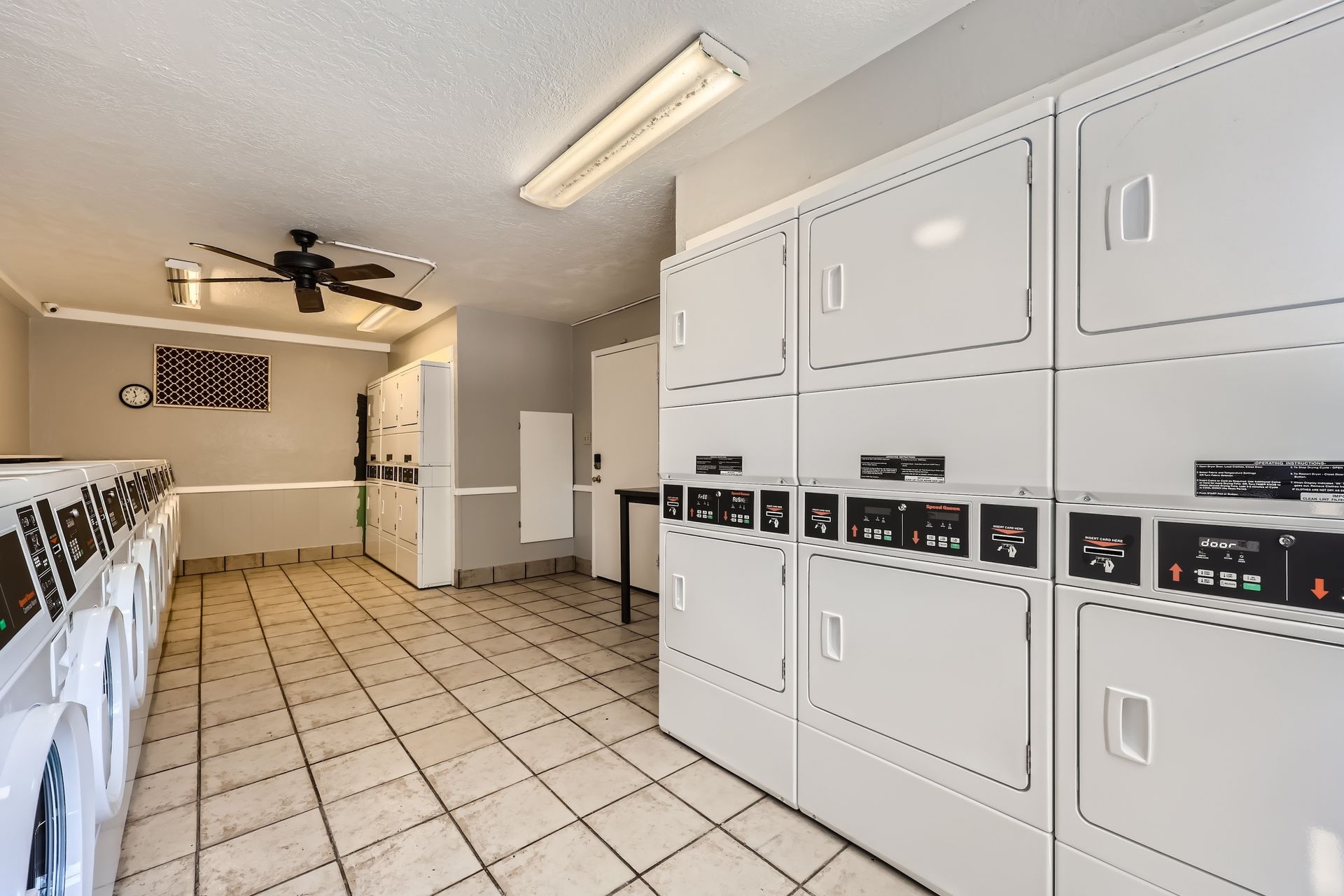 Laundry room with white washers and dryers, tiled floor, and a ceiling fan.