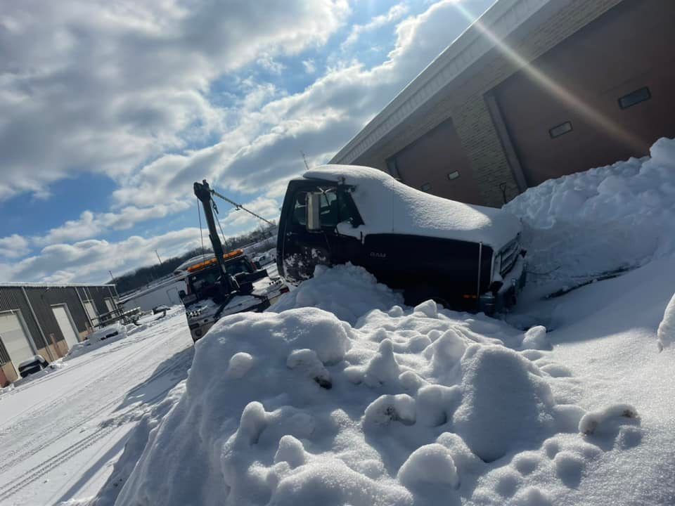A tow truck pulling a dark-colored vehicle from a snowdrift beside a building on a snowy day.