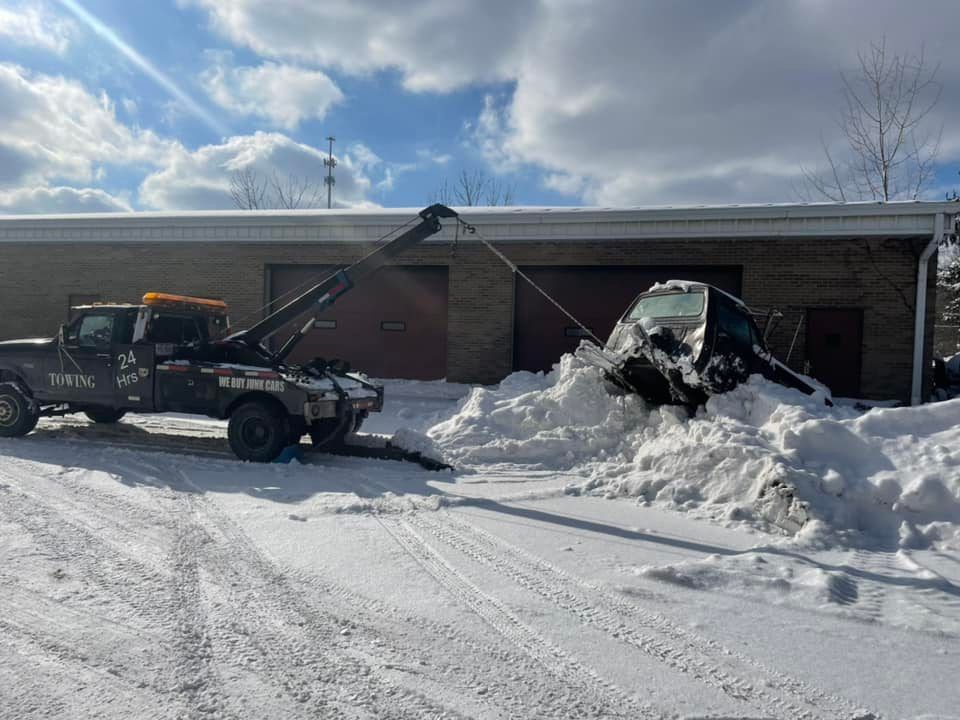 Tow truck pulling a car out of a snow bank. The scene is outdoors with a building in the background.