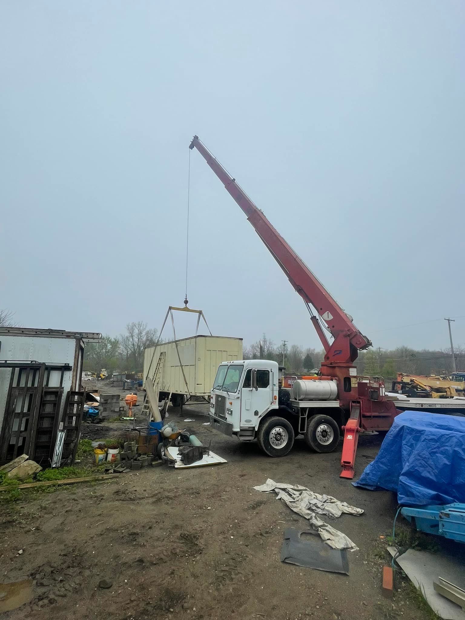 Crane lifting a large, tan container in a construction area on a cloudy day.
