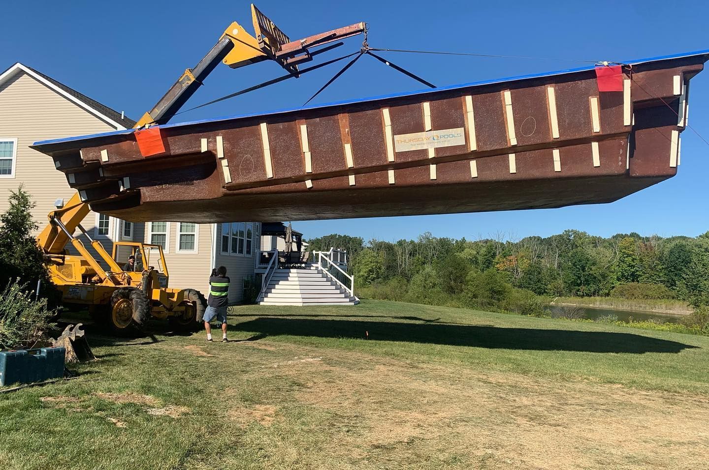 A forklift lifting a large, brown rectangular structure, possibly a pool, near a house.