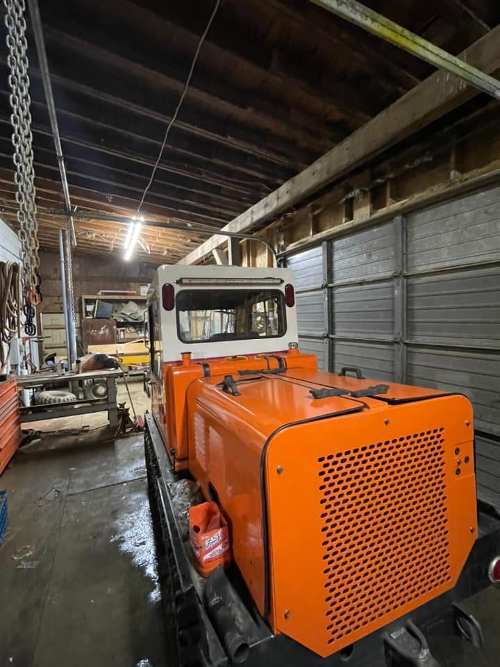 Orange industrial vehicle inside a workshop with wooden beams and a white cabin.