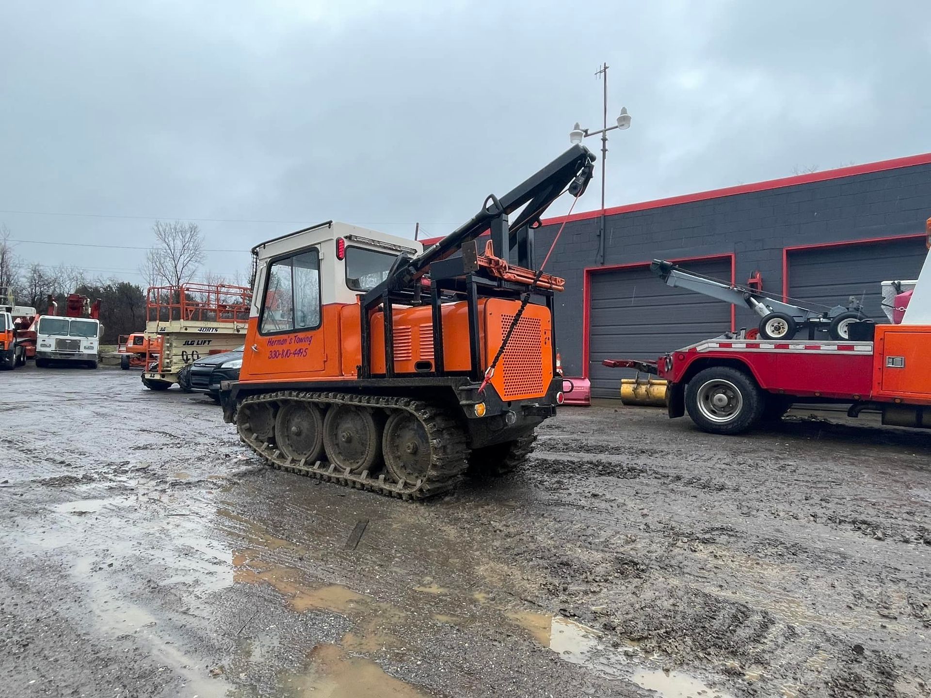 Orange tracked vehicle with a crane on muddy ground.