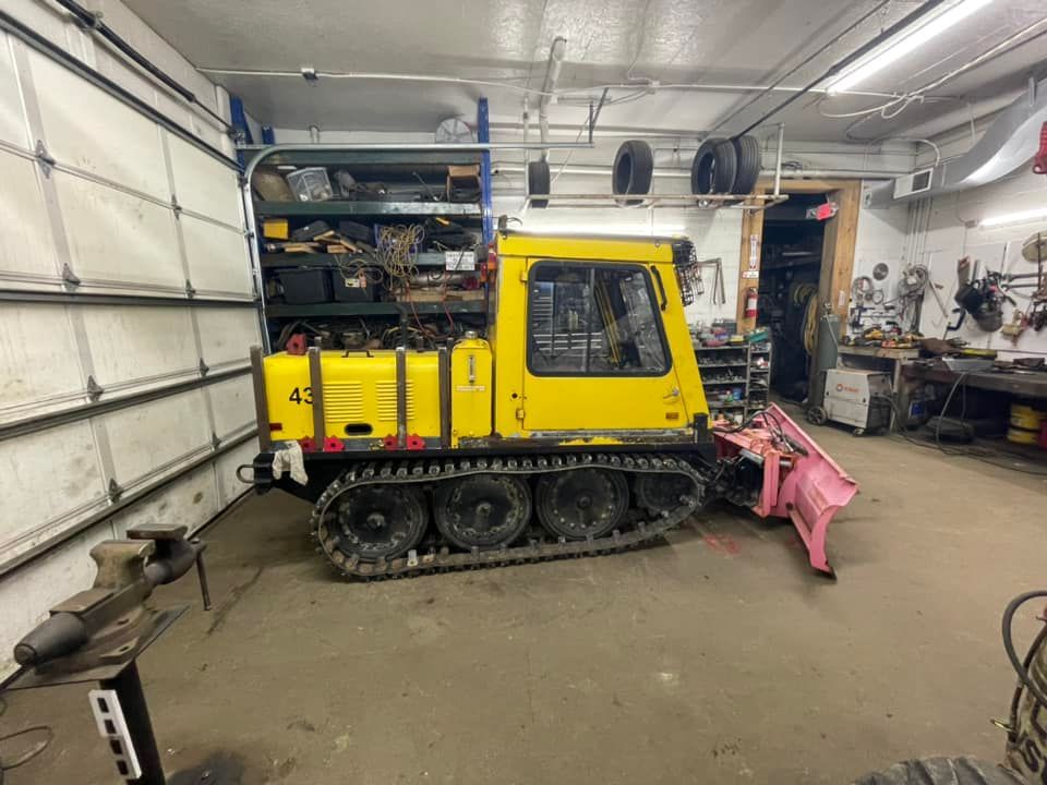 Yellow tracked vehicle with pink snowplow in a workshop.