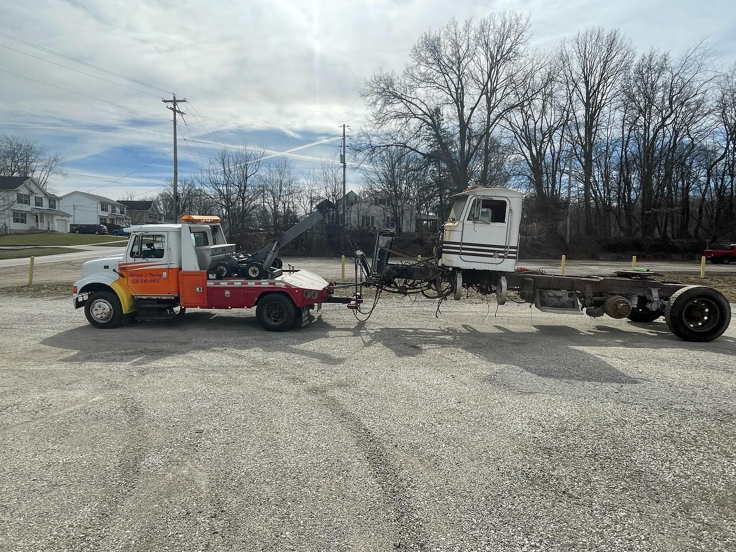 Tow truck hauling a truck cab and chassis on a gravel lot under a cloudy sky.