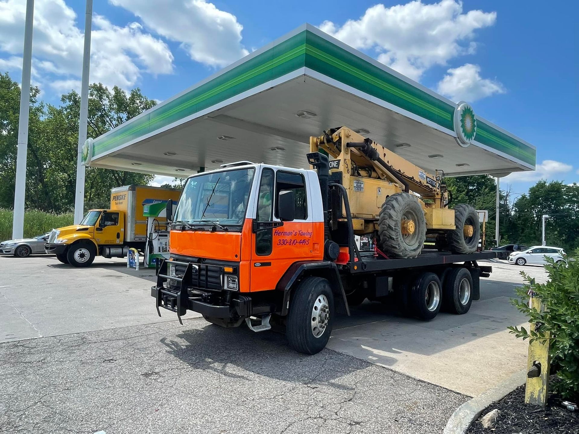 Tow truck lifting a large tree trunk. The truck is red and black, outdoors in a grassy area.