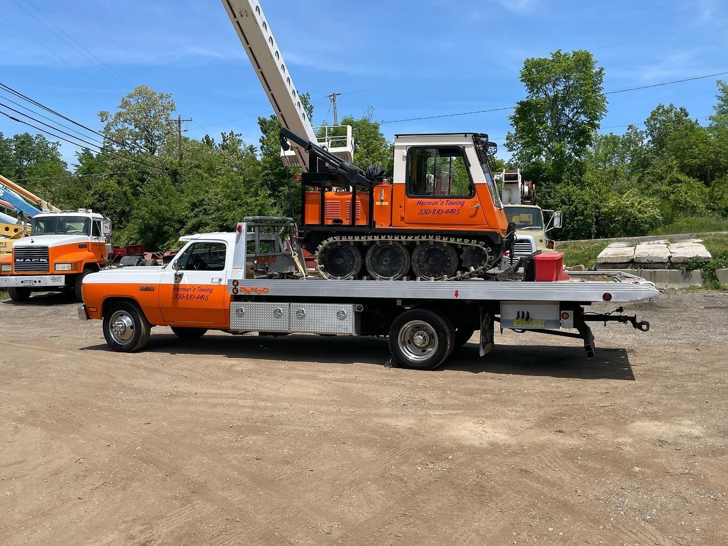 Orange tow truck transporting an orange tracked vehicle on a sunny day.