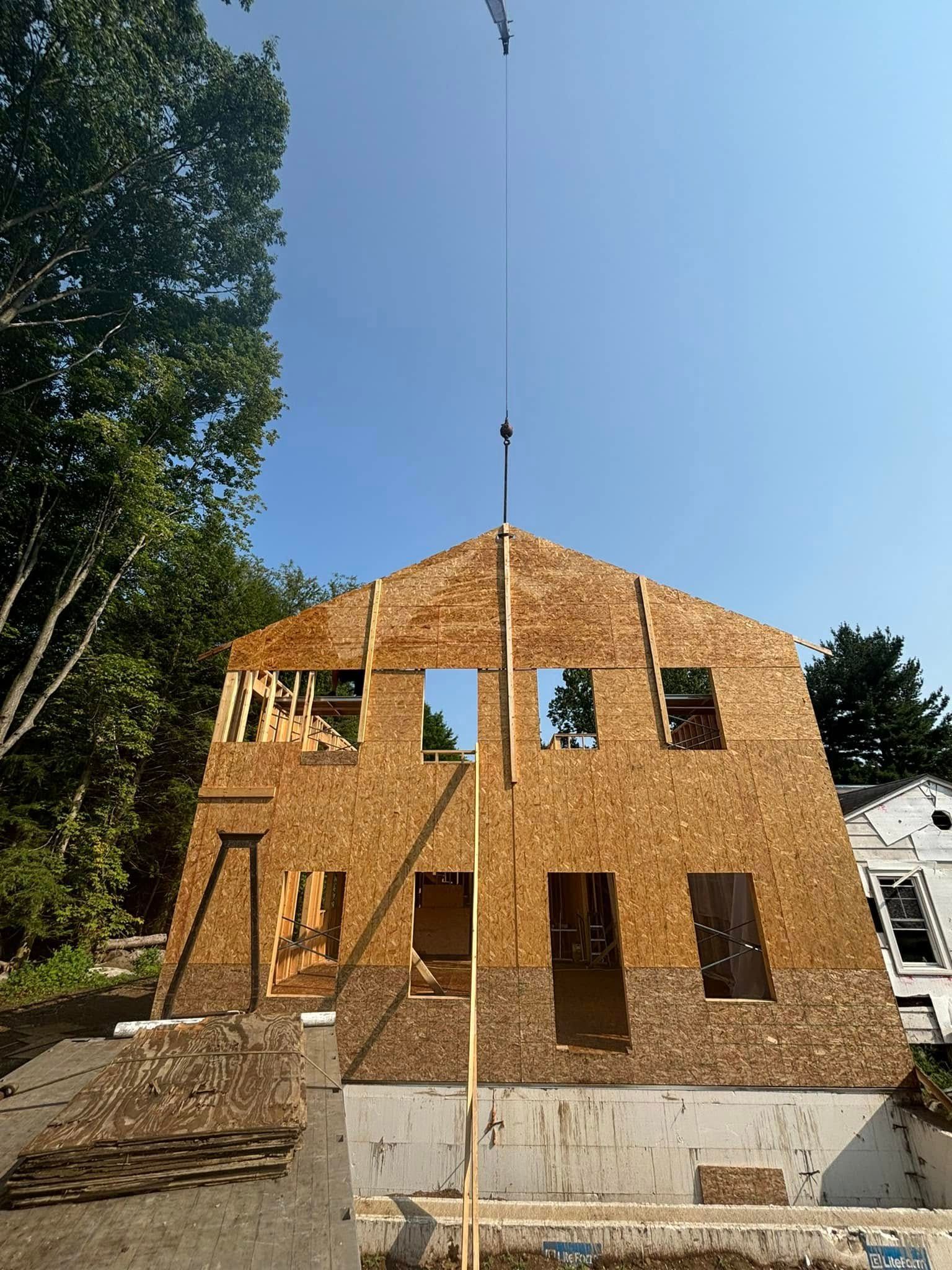 House under construction with a crane overhead on a sunny day. OSB siding, framed windows and doors.