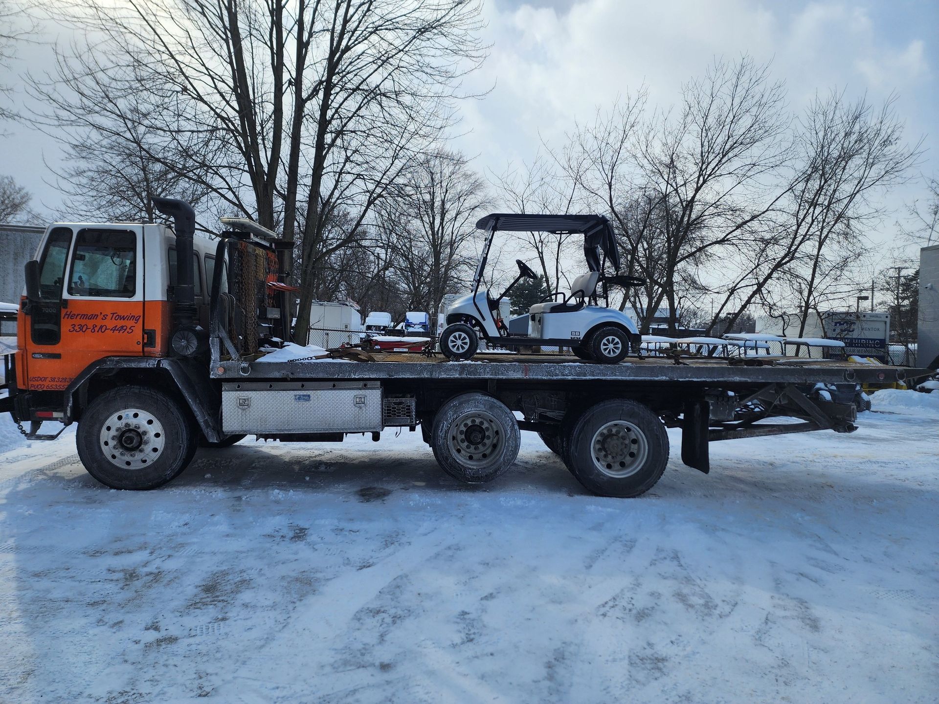 Tow truck transporting a white golf cart on a snowy day.