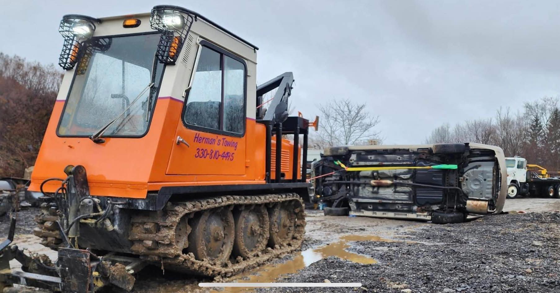 Orange tracked vehicle next to an overturned white truck on a muddy lot.
