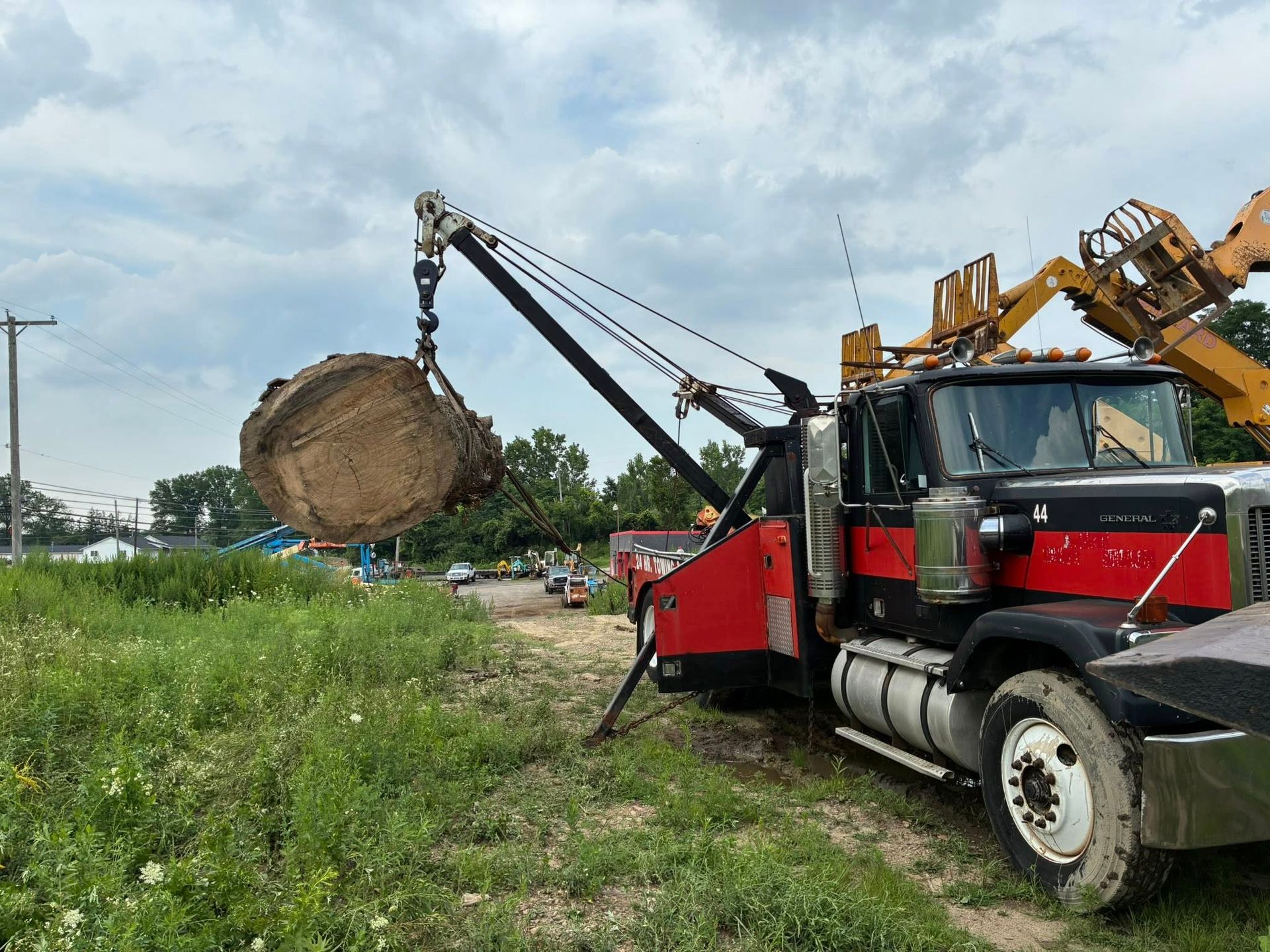 Tow truck lifts a large, round, dirt-covered object in a grassy field on a cloudy day.