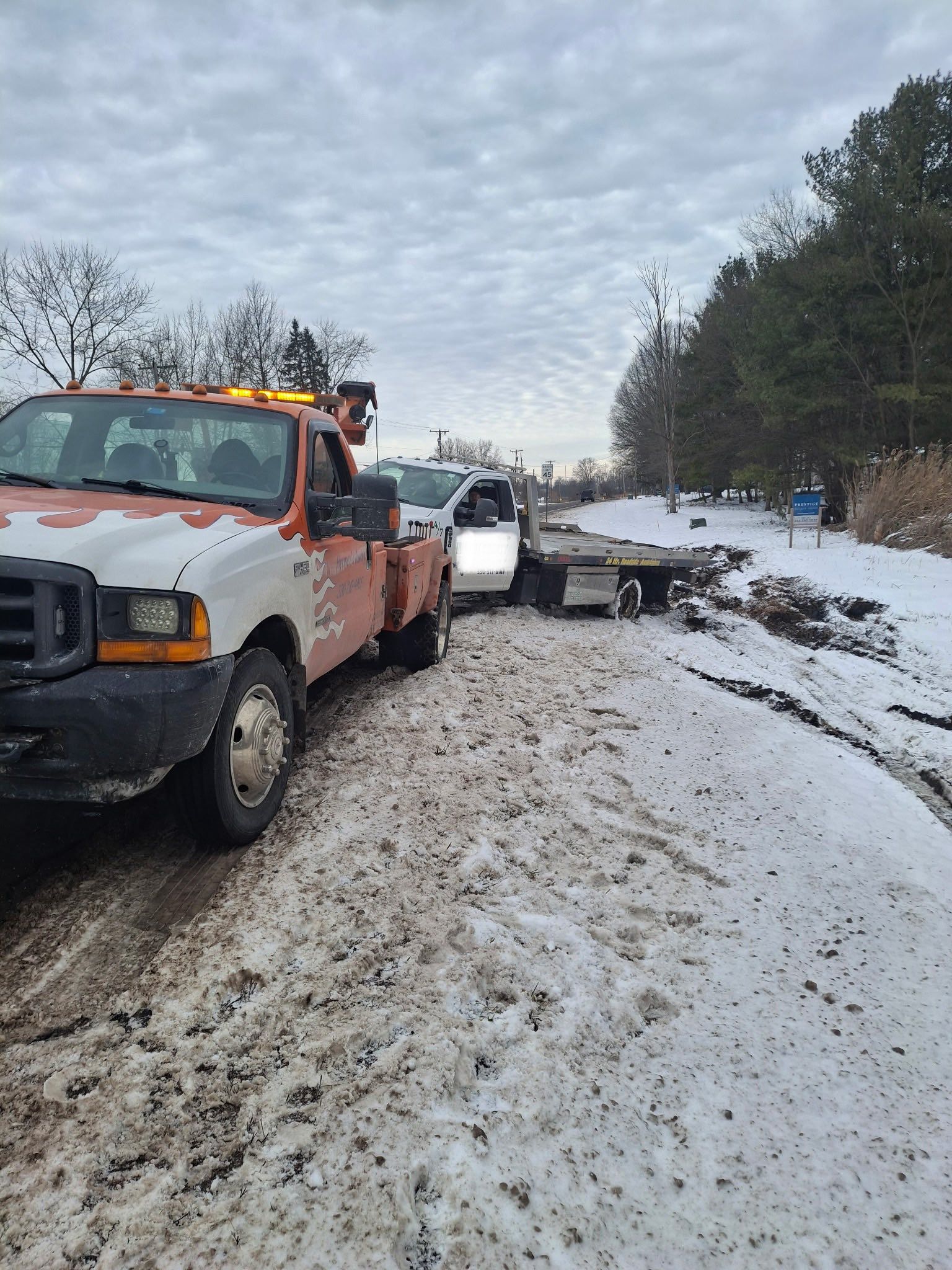 Tow truck pulling a vehicle from snow-covered roadside. Overcast sky.