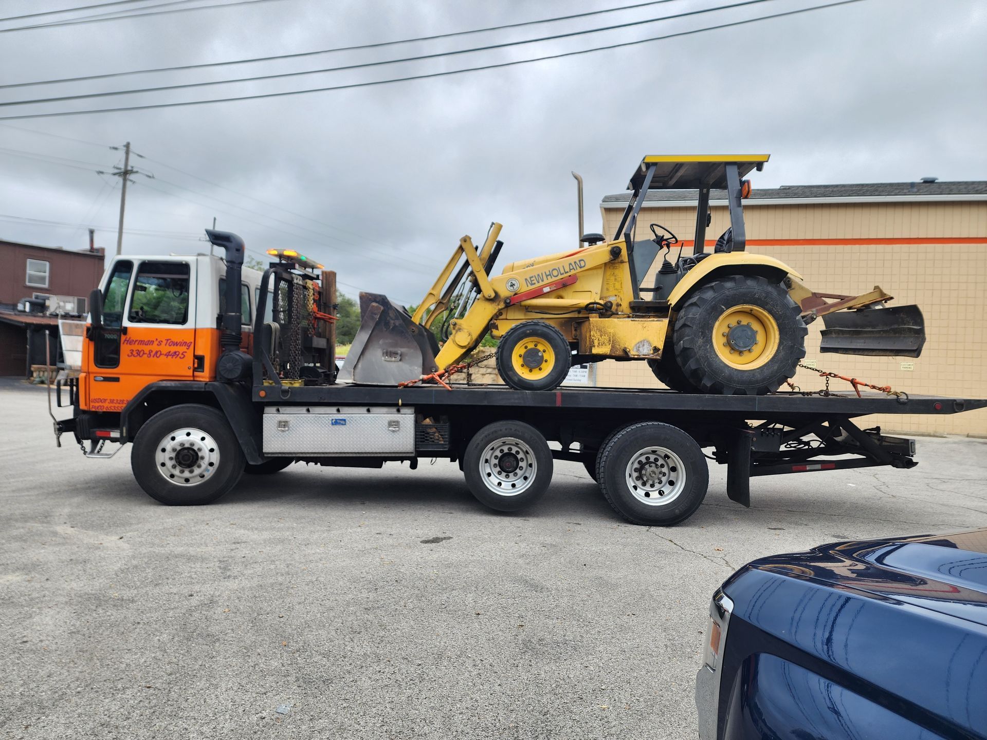 Yellow tractor on a flatbed tow truck. Gray sky, industrial setting.