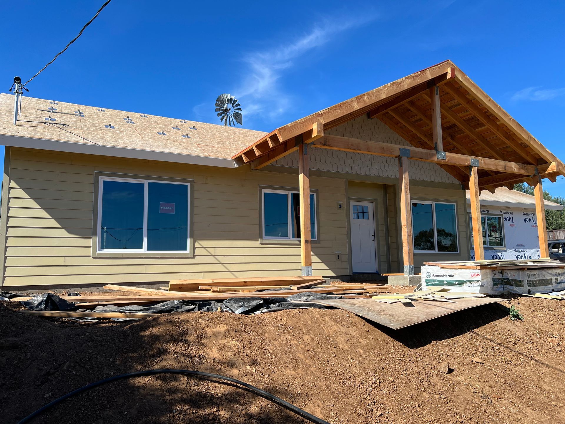 House under construction with tan siding, a covered porch, and a clear blue sky.