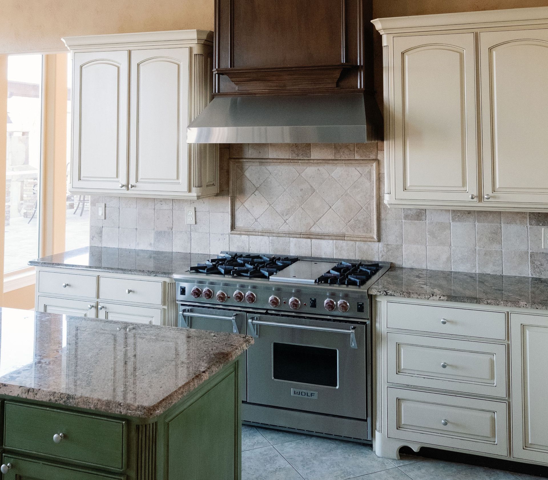 Kitchen with cream cabinets, stainless steel range, brown tile backsplash, and granite countertops.