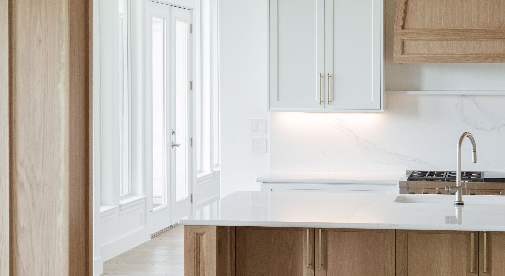 Modern white and wood kitchen with island, cabinets, and large windows.