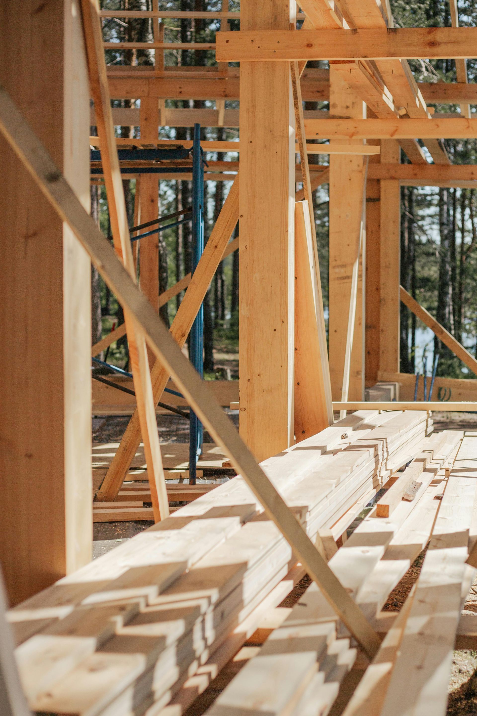 Wooden house frame under construction in a sunny forest, beams and planks visible.