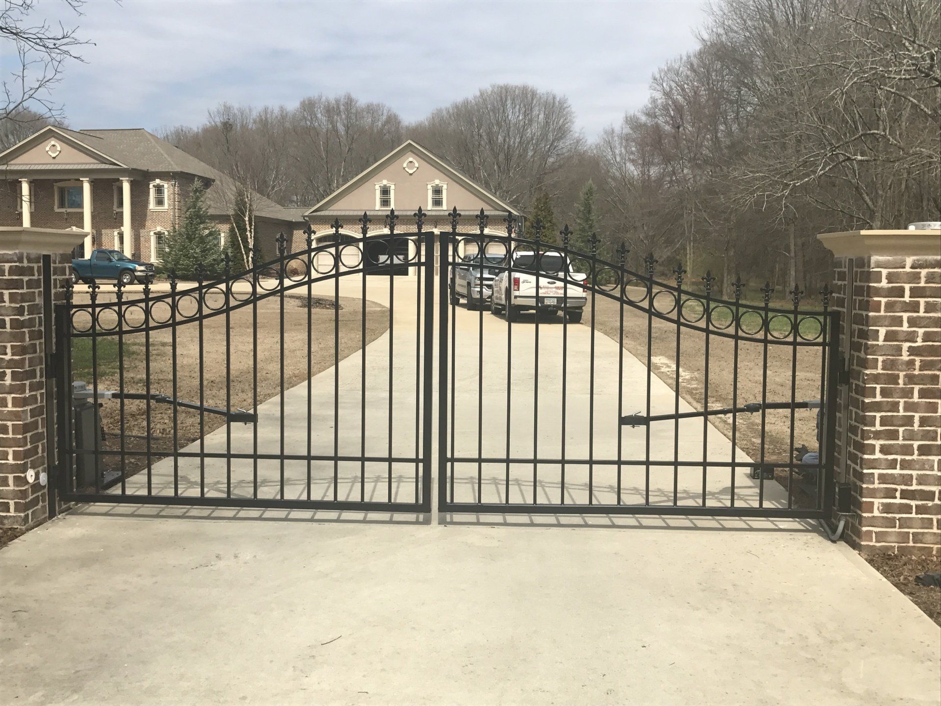 A wrought iron gate is open to a driveway leading to a large house.