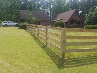A wooden fence surrounds a lush green yard in front of a house.