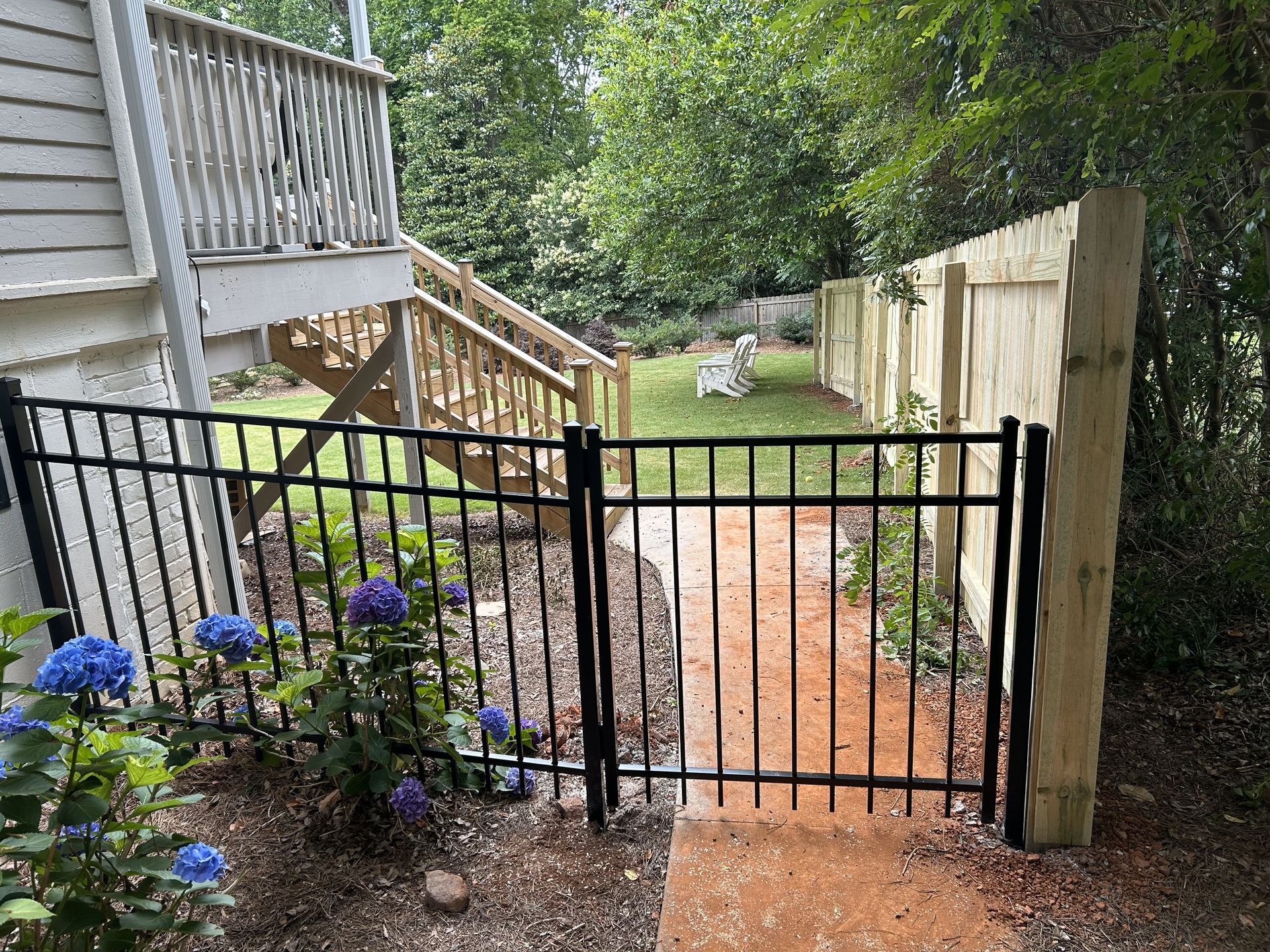 A black fence surrounds a yard with a wooden deck and stairs.