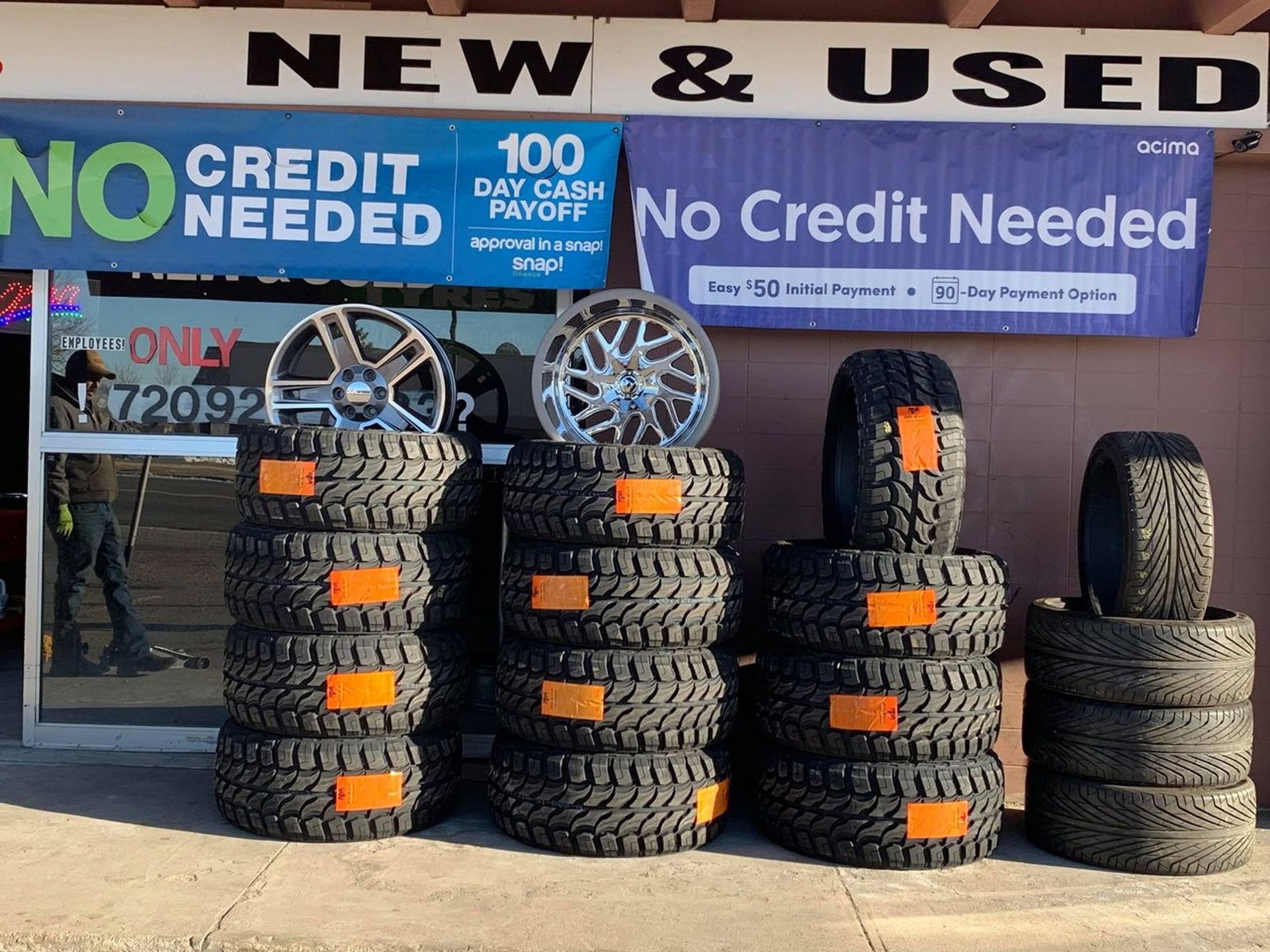 Tires are stacked in front of a store that says new and used
