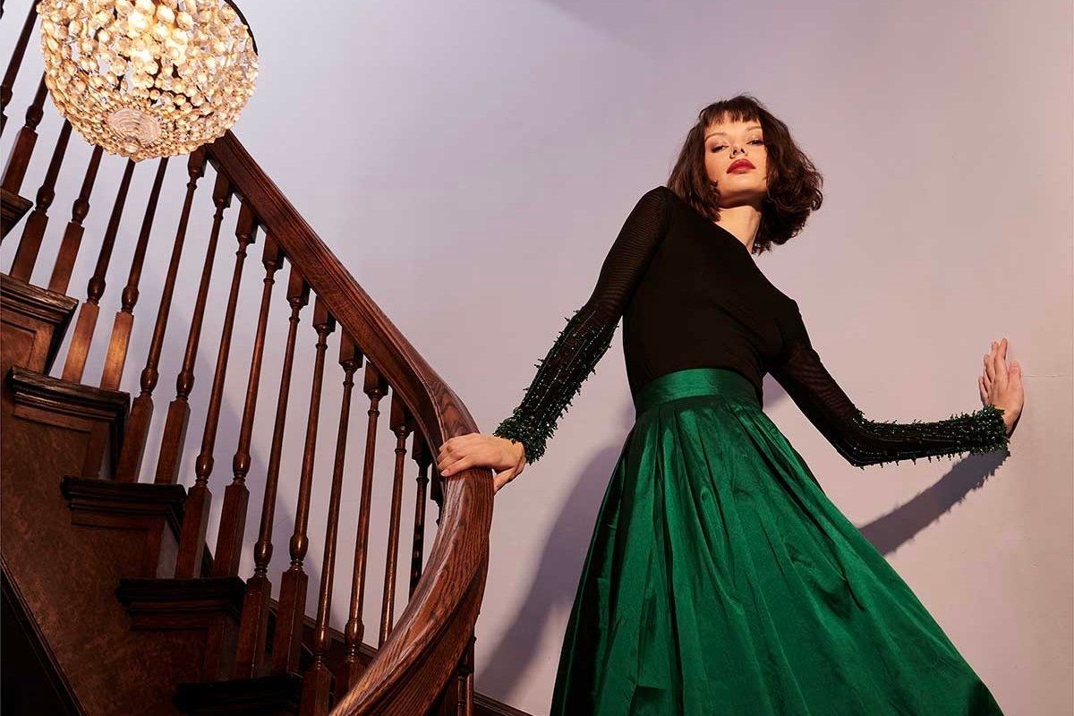 A woman in a green dress is standing on a wooden staircase.