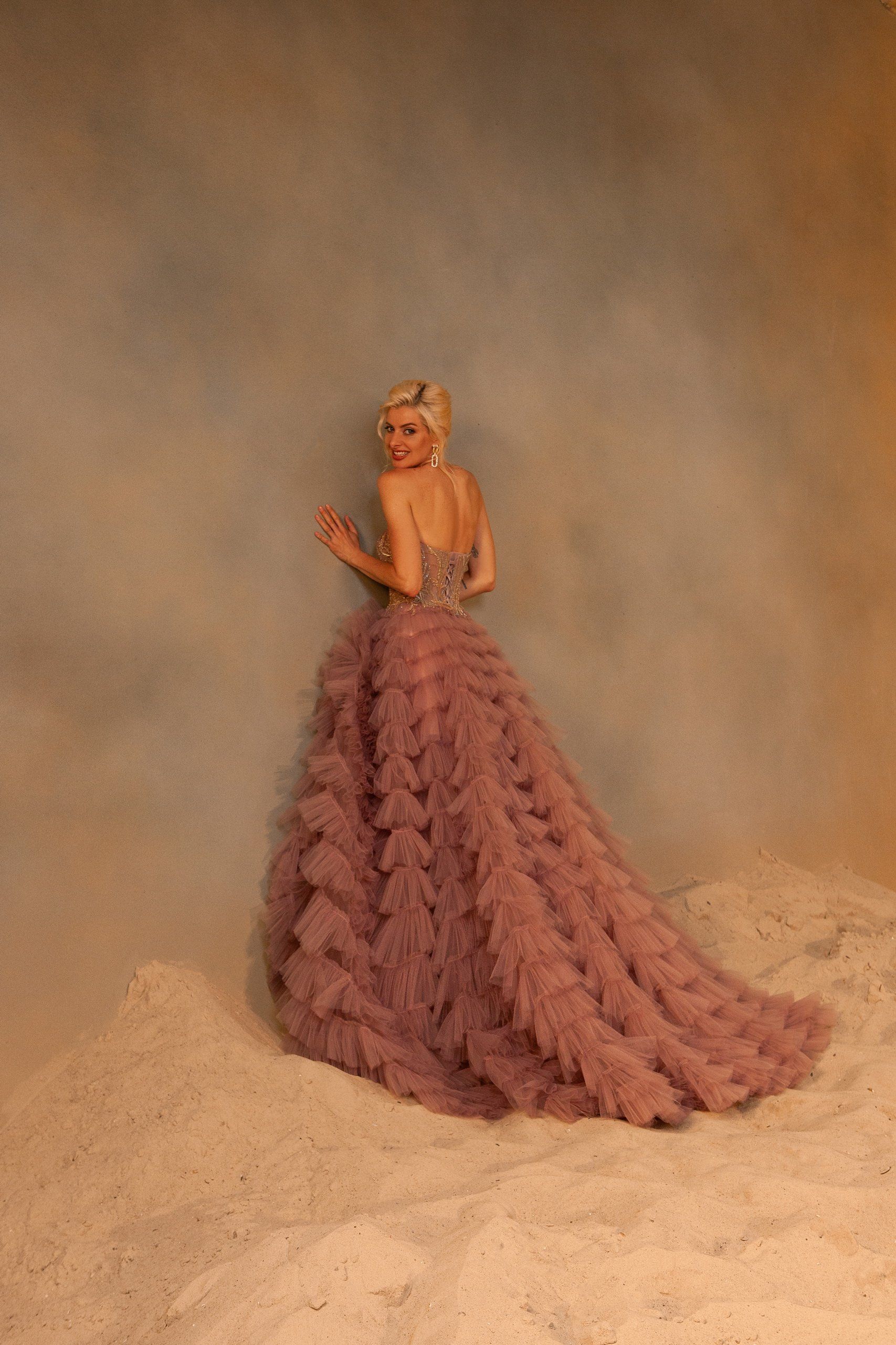 A woman in a long pink dress is standing in the sand.