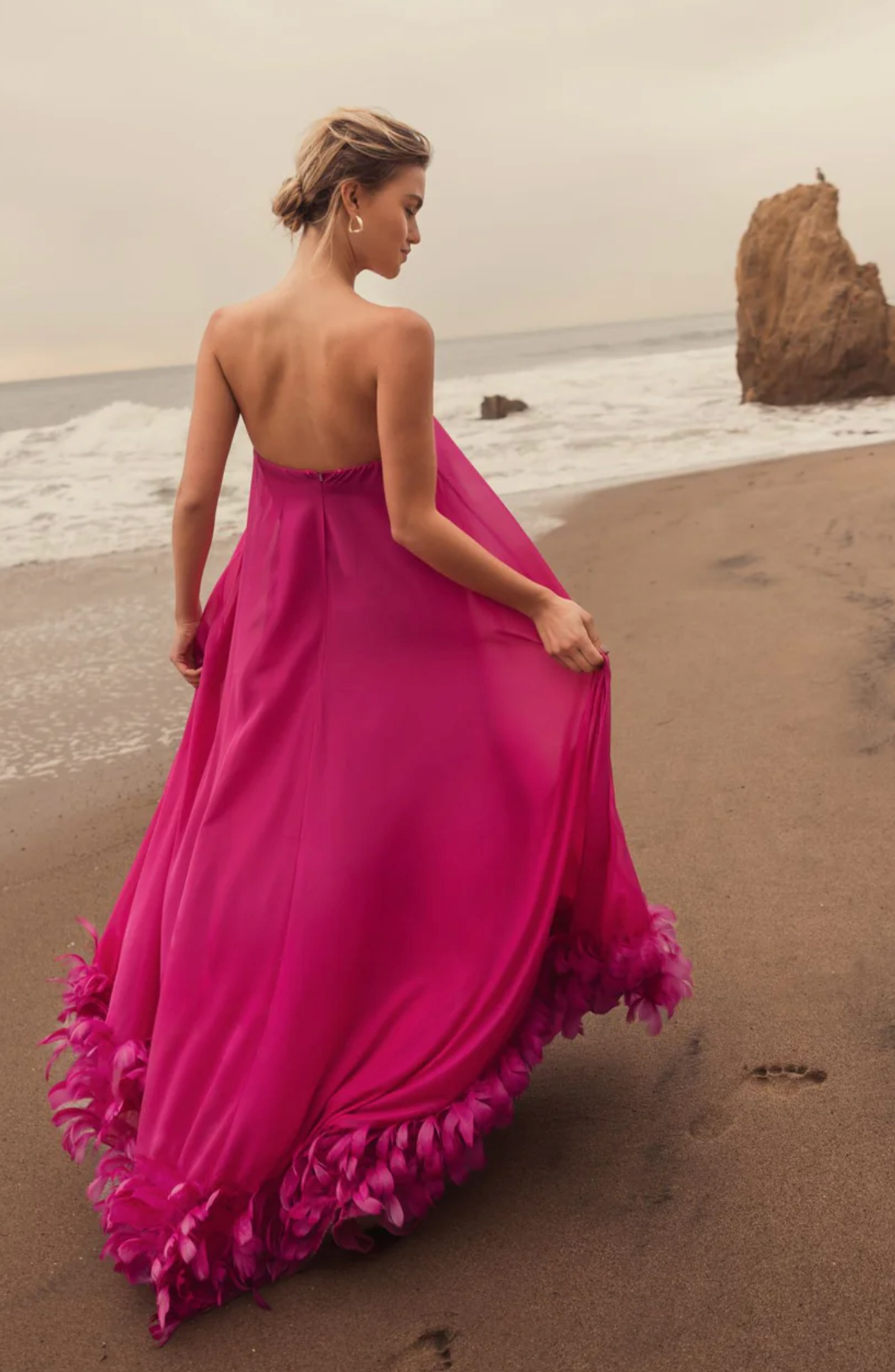 A woman in a long pink dress is walking on the beach.