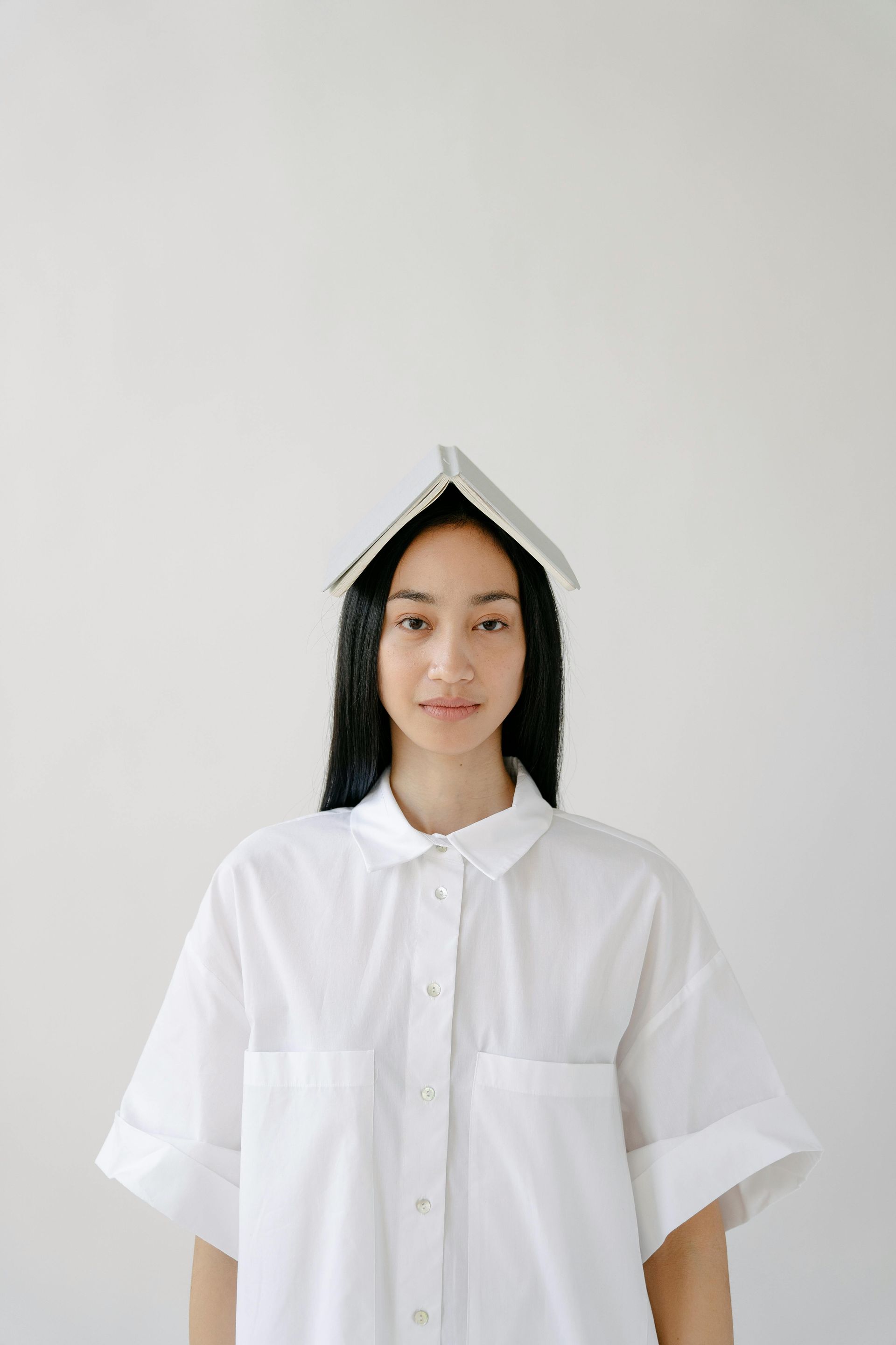 A woman in a white shirt is holding a book on her head.