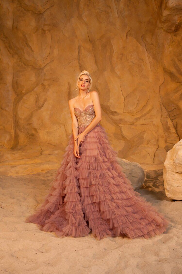 A woman in a pink dress is standing in front of a rock formation.